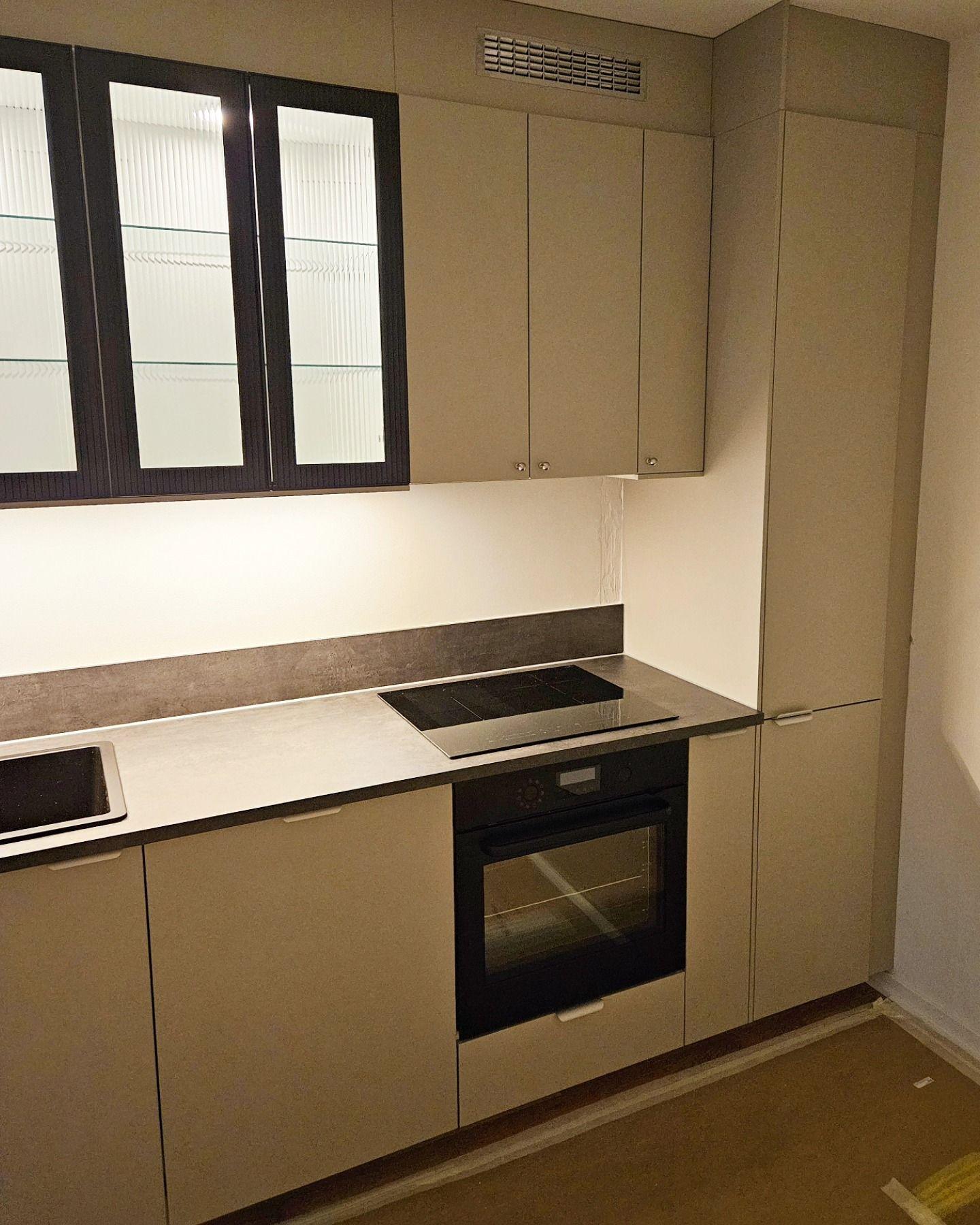 Kök med beige luckor, betongfärgad bänkskiva, inbyggd ugn och induktionshäll
