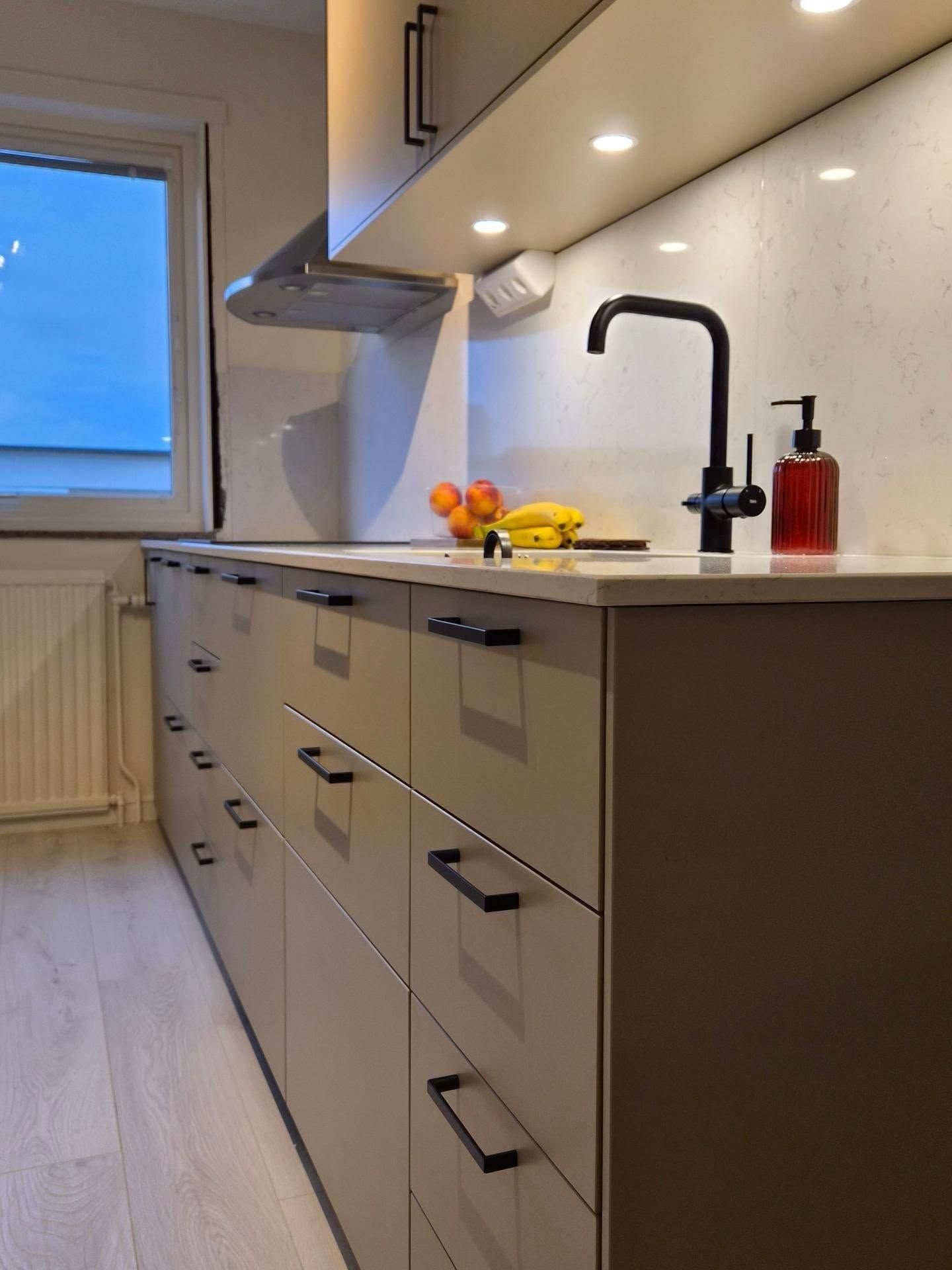 Närbild på bänkskiva, svart blandare och beige lådfronter
