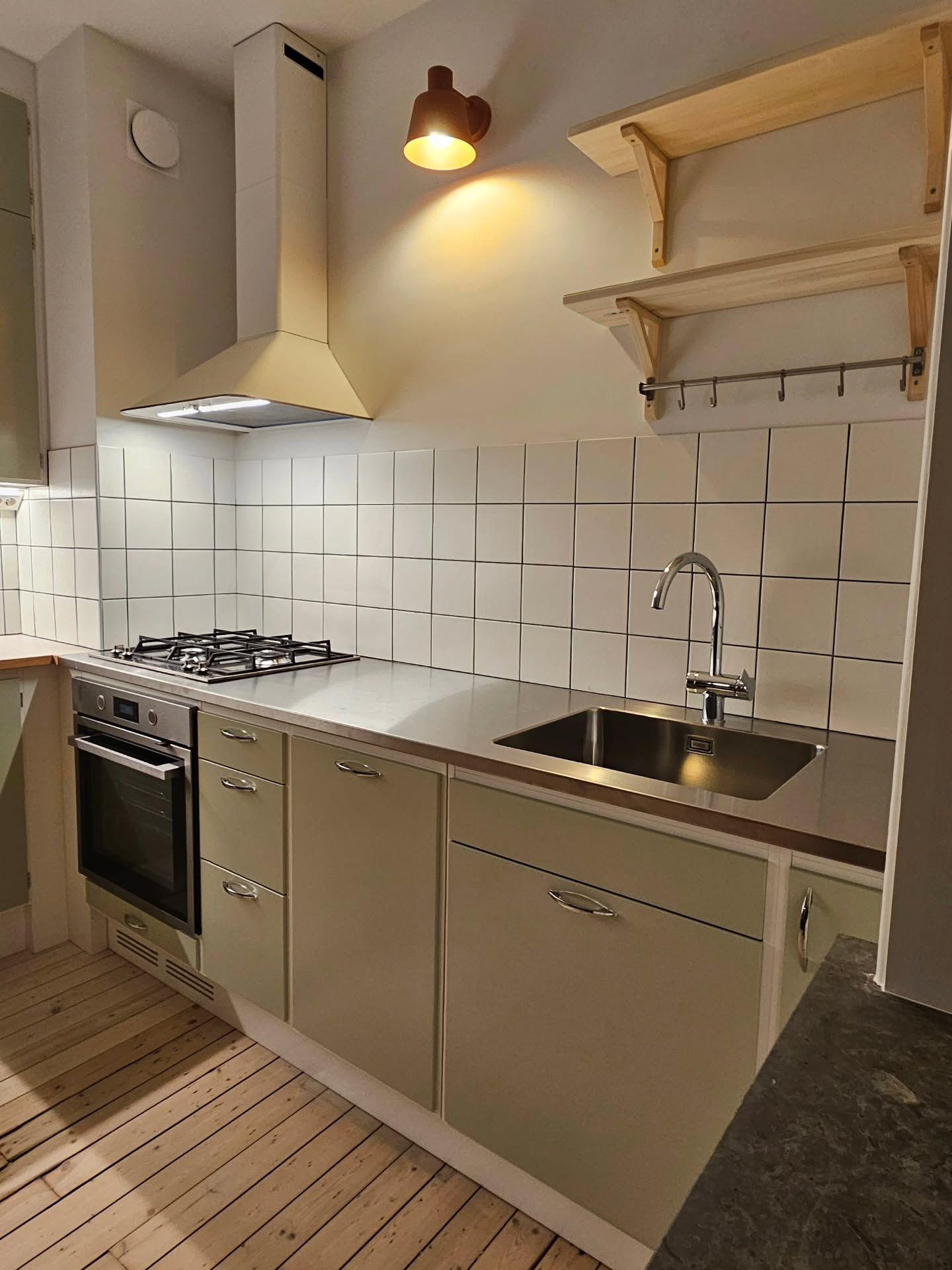 Köket sett från sidan med spiskåpa, diskho och trägolv