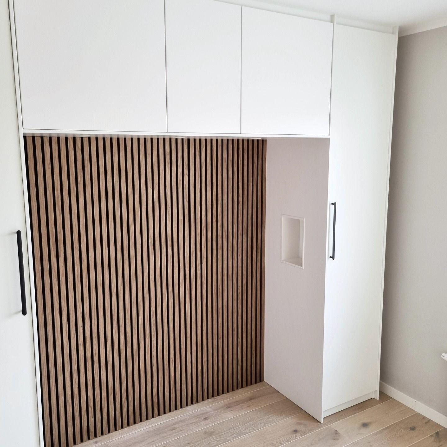 Vit platsbyggd garderob med överskåp och infälld nisch med ribbpanel i ek