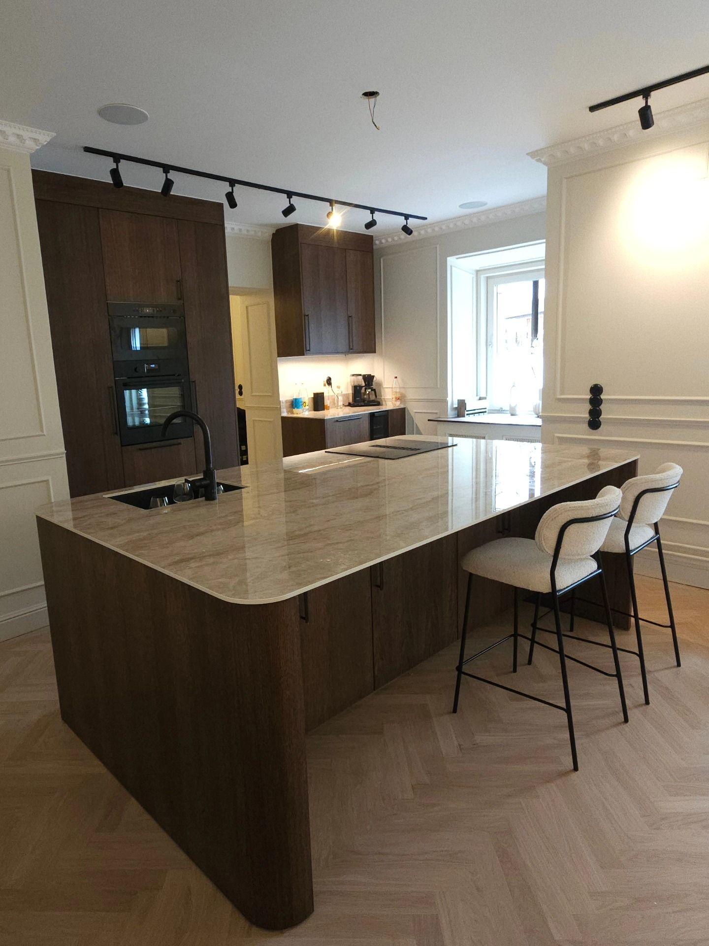Köket sett från sidan med köksö, barstolar och fönster