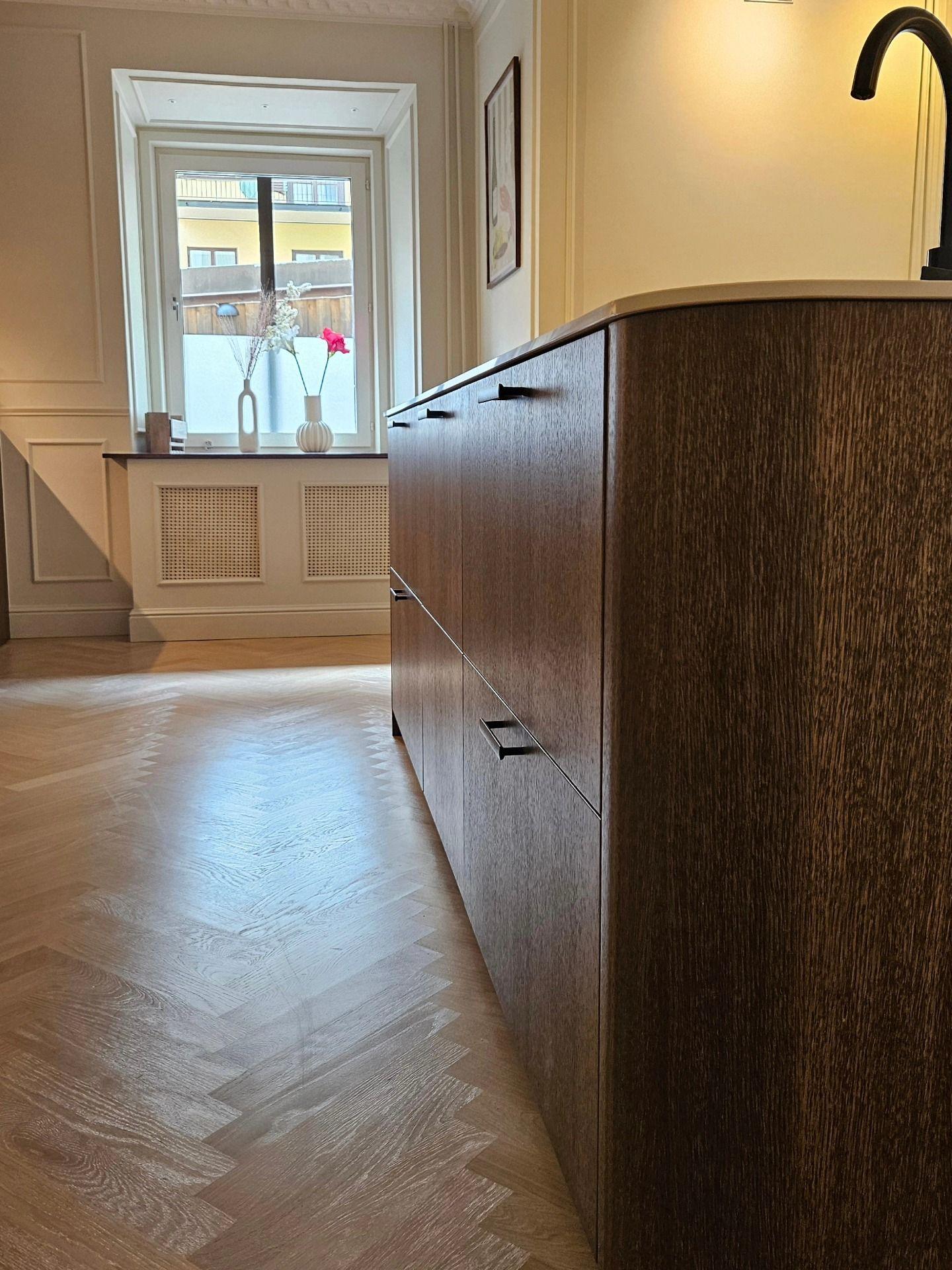 Köksöns lådfronter i mörk ek med fiskbensparkett och fönster med radiatorkåpa