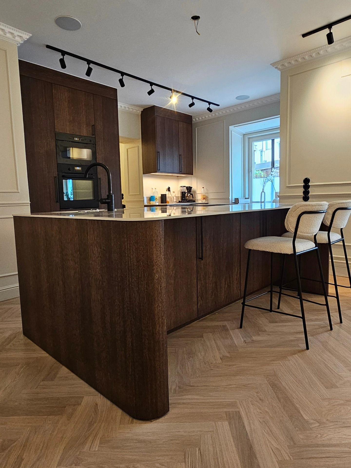 Köket med högskåp, inbyggd ugn och barstolar vid köksön