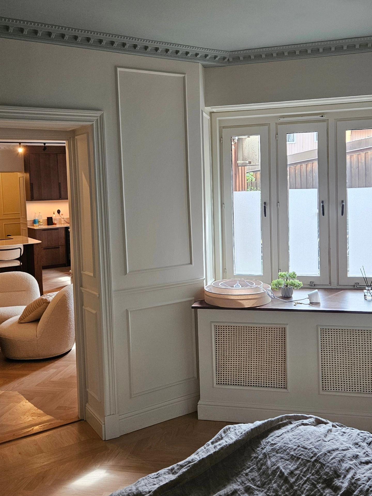 Sovrum med väggfält, dörröppning mot kök och fönsternisch med radiatorinklädnad