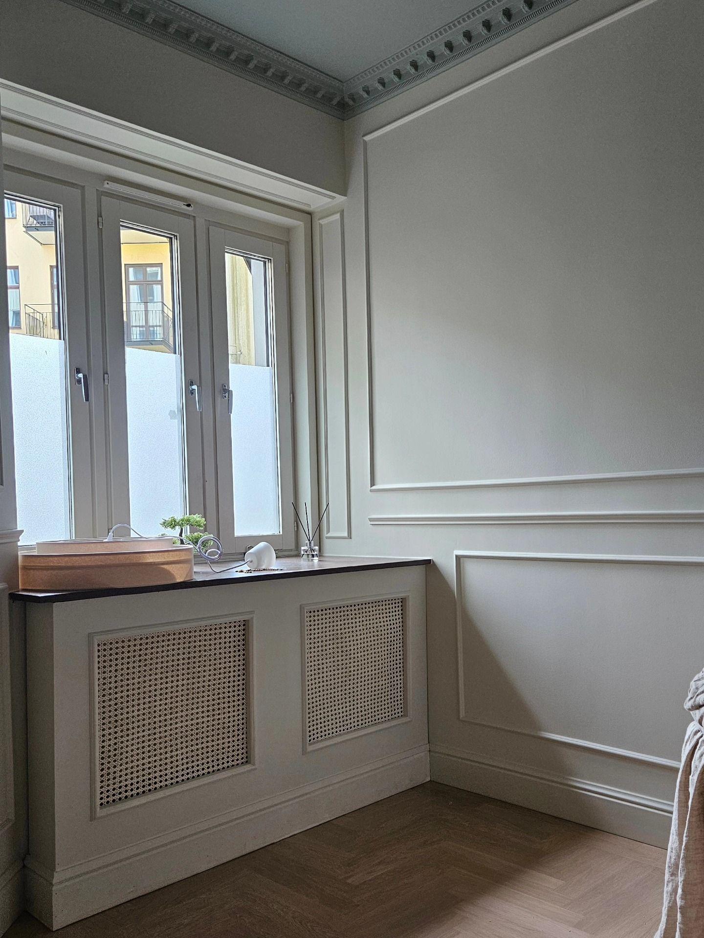 Fönsternisch med rottingfronter och mörk fönsterbänk mot panelad vägg