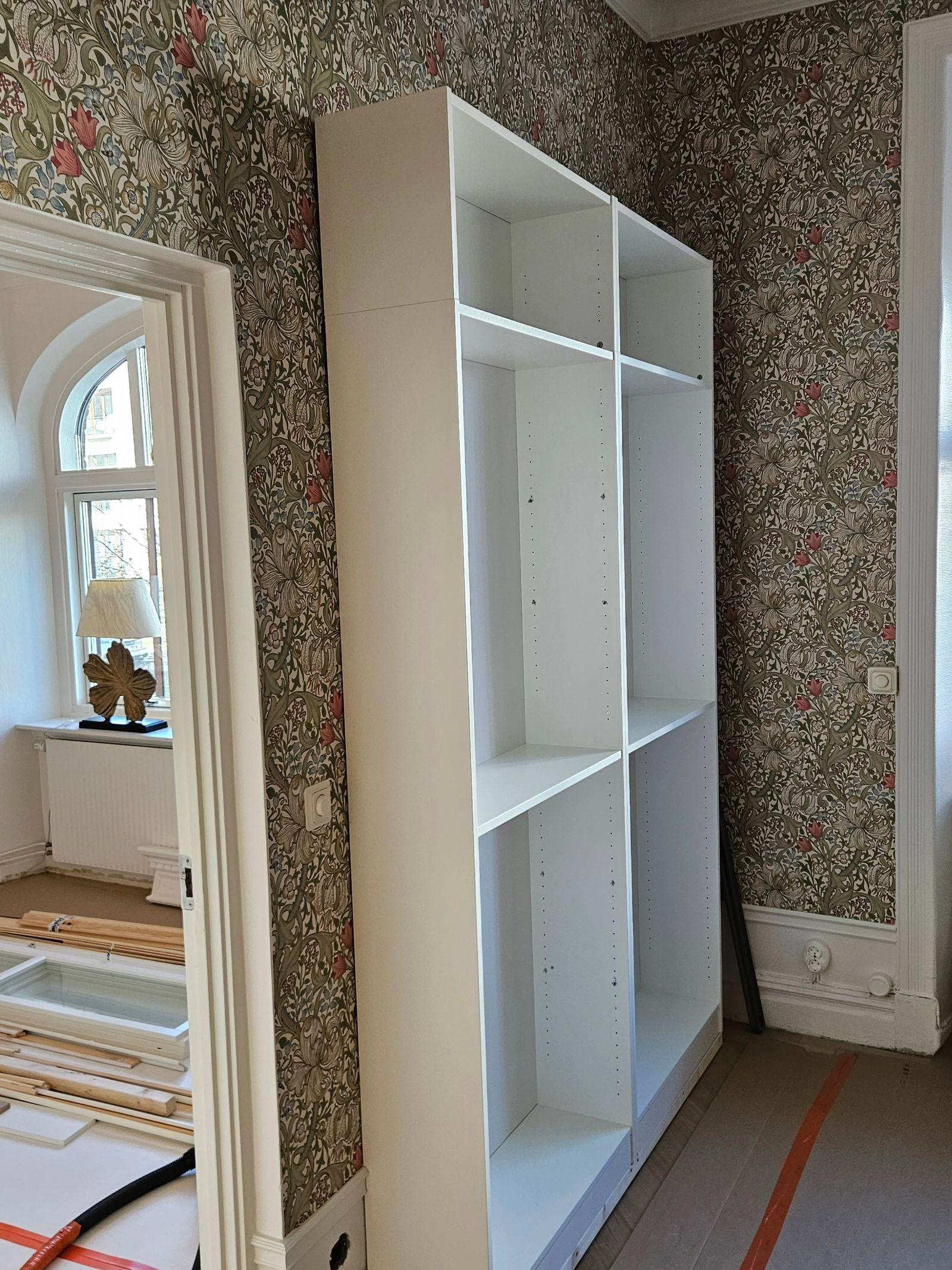 Vita hyllstommar uppställda mot mönstrad tapet under montering