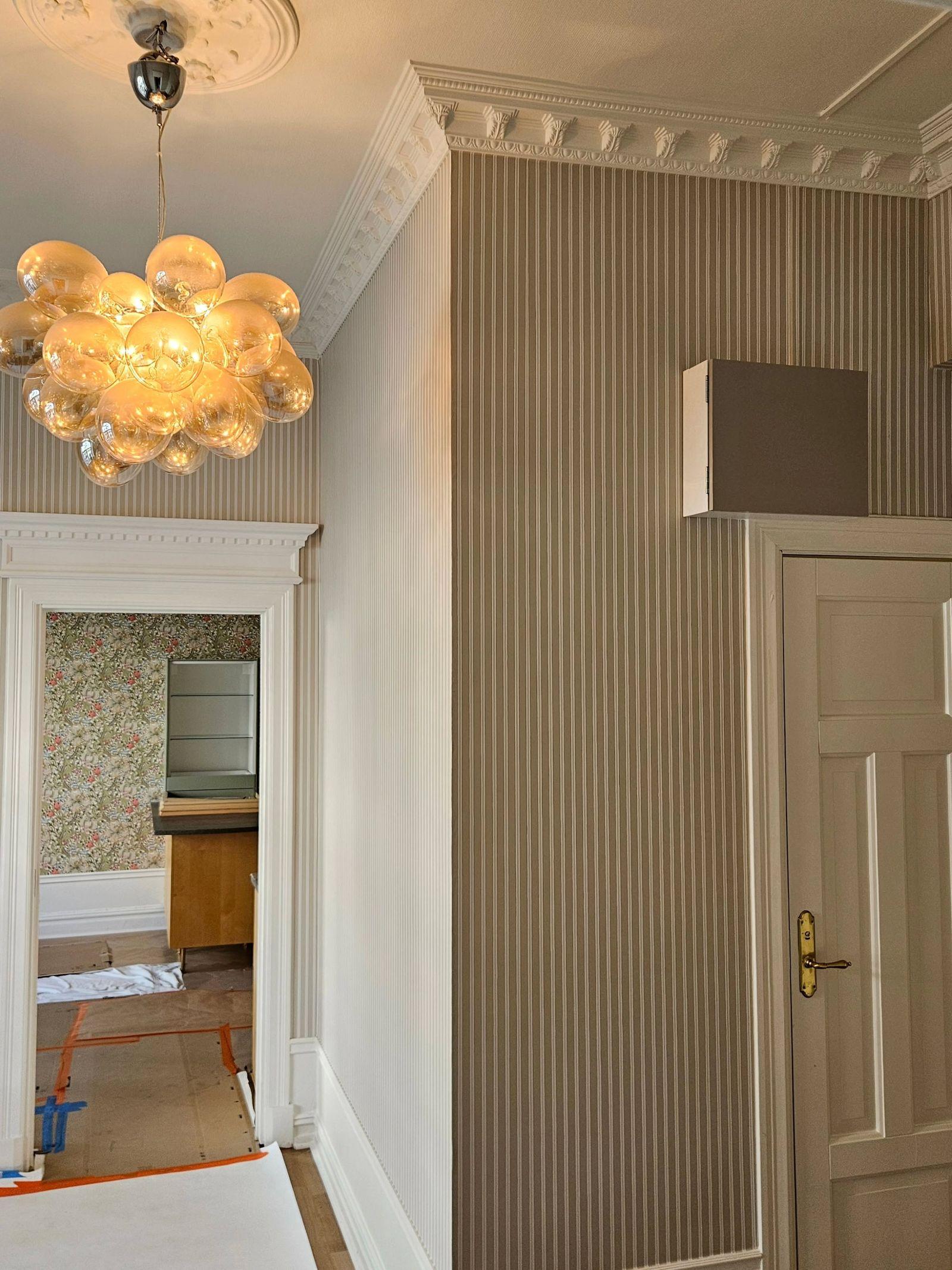 Hall med randig tapet, vita stucklister och taklampa i glas