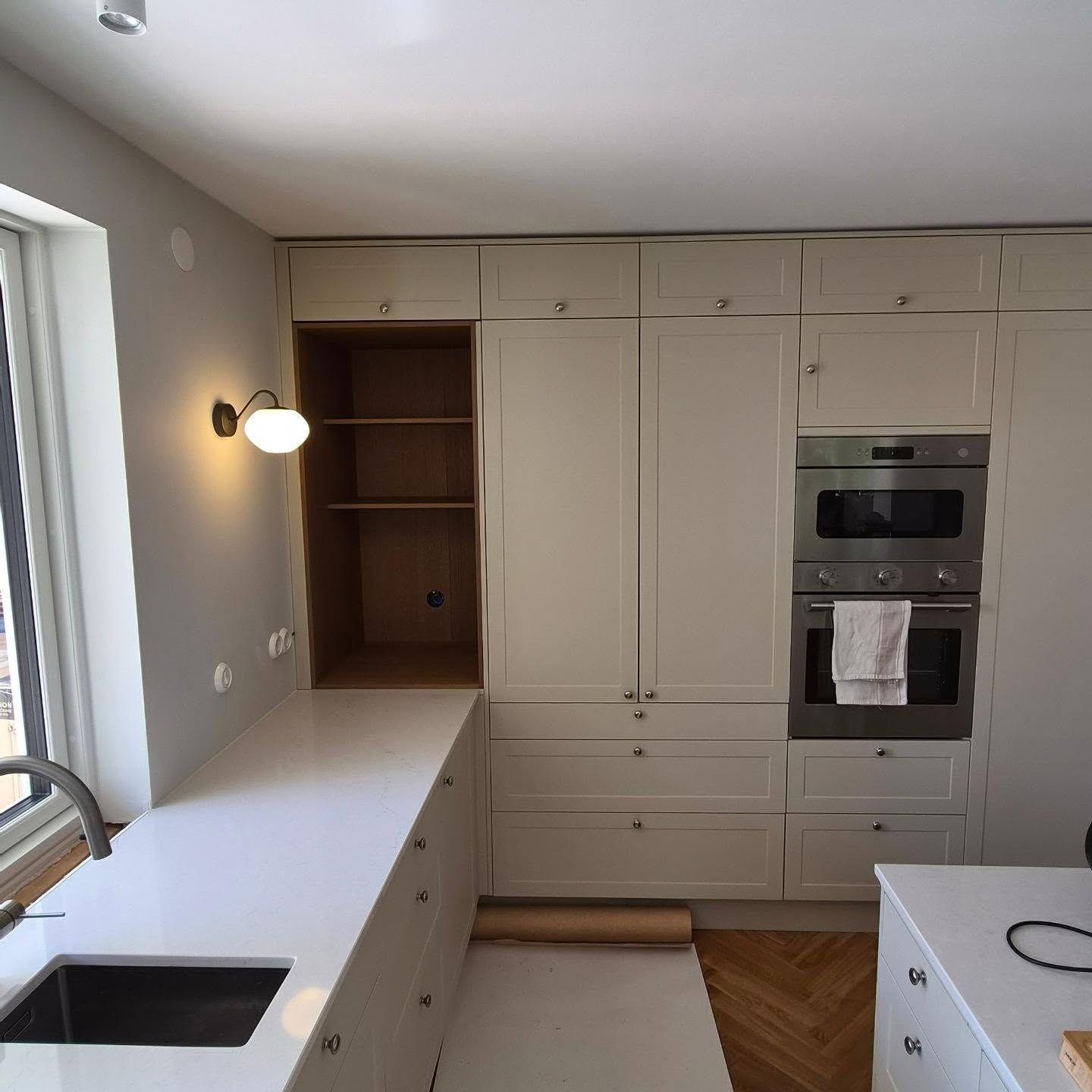 Köket med inbyggda högskåp, ugnar och ljus bänkskiva