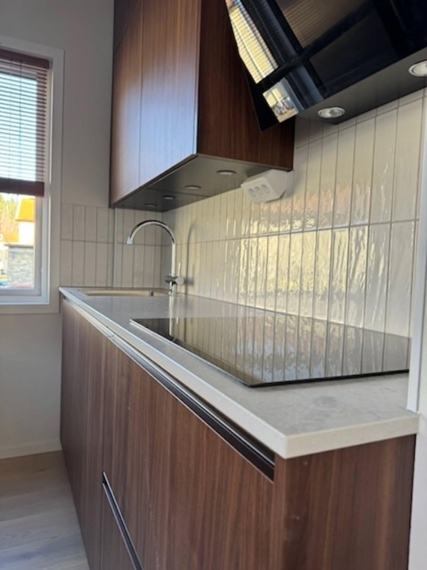 Vy längs bänkskivan med induktionshäll och vitt stående kakel