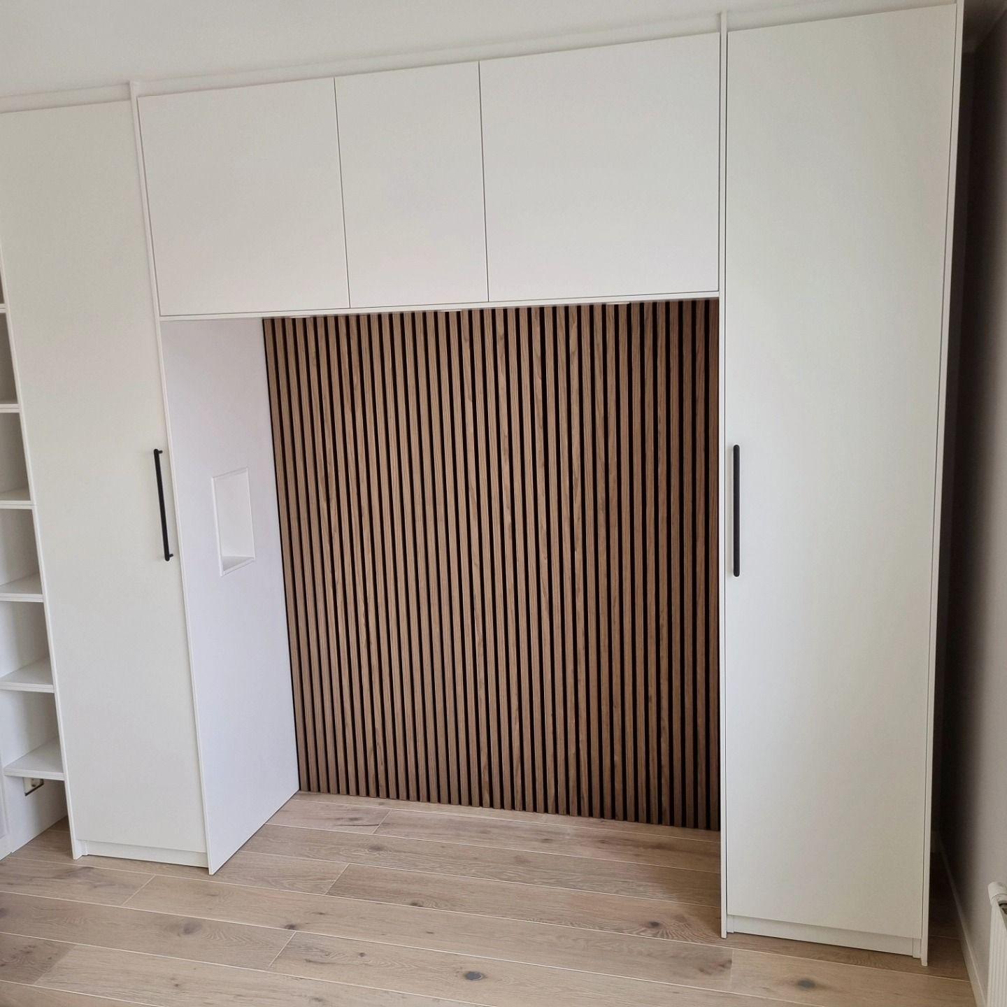 Garderobsvägg i vitt med ribbpanel i ek och svarta stånghandtag